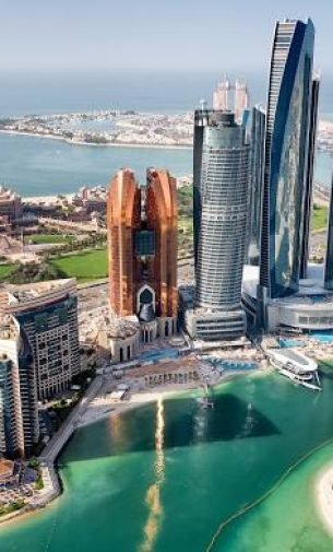 An aerial view of the Abu Dhabi skyline featuring the prominent Etihad Towers and Khalidiya Palace buildings, with a waterfront and clear blue sky.